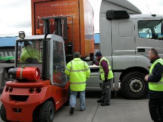 three_workers_in_hi-viz_jackets_supervising_a_forklift_truck_loading_a_container_onto_a_HGV_trailer