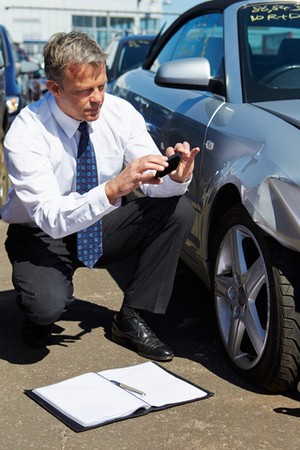 post accident rehabilitation course man with camera kneeling by  car to assess collision damage to the front wing
