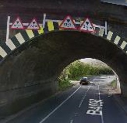 a_low_railway_bridge_over_a_road_showing_four_restricted_height_triangular_warning_signs