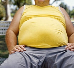 a_seated_overweight_man_in_yellow_T_shirt_and_grey_trousers.
